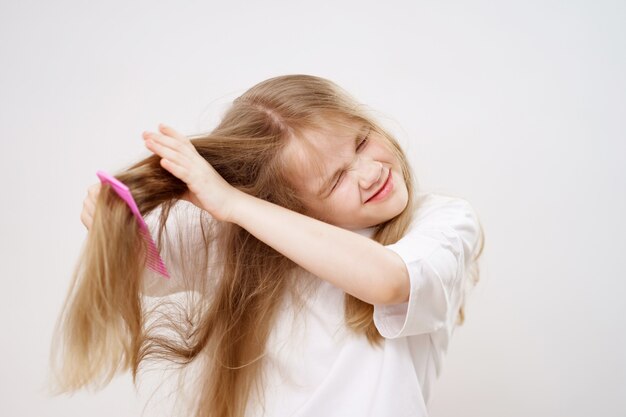 Niña peina el cabello enredado sobre un fondo blanco cosméticos para el  cuidado del cabello de los niños  Foto Premium